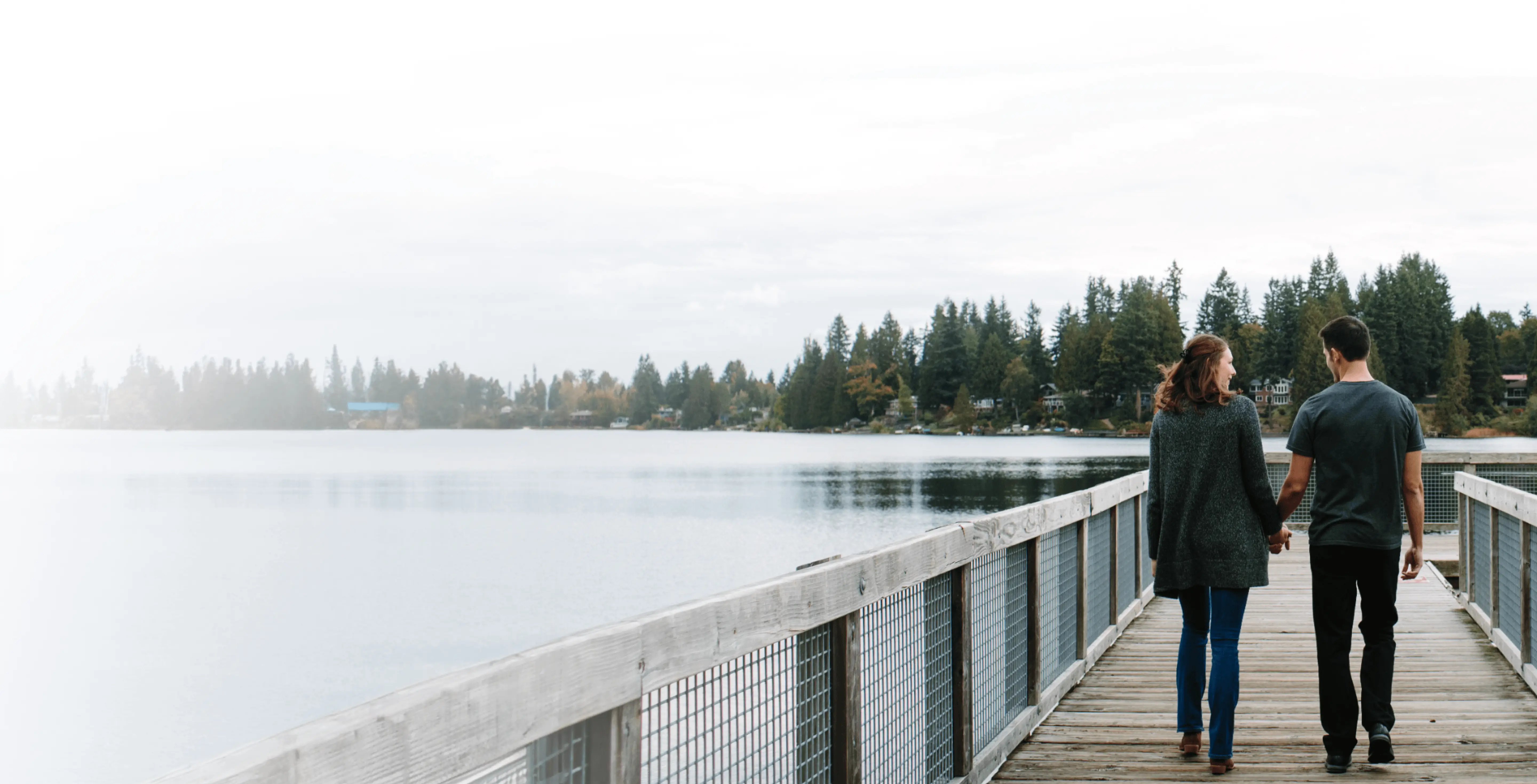 A man and woman holding hands and walking on a dock on a lake