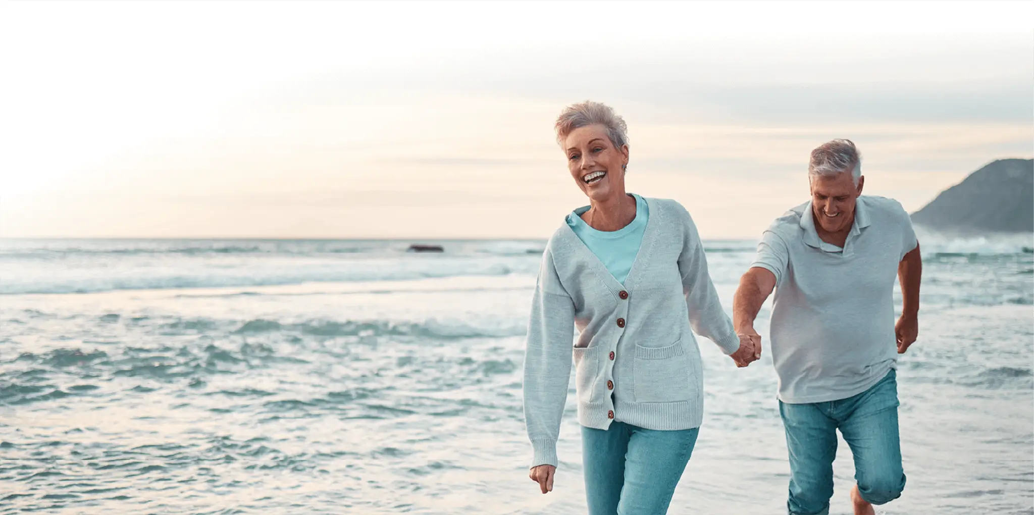 A couple smile and hold hands as they walk along the beach.