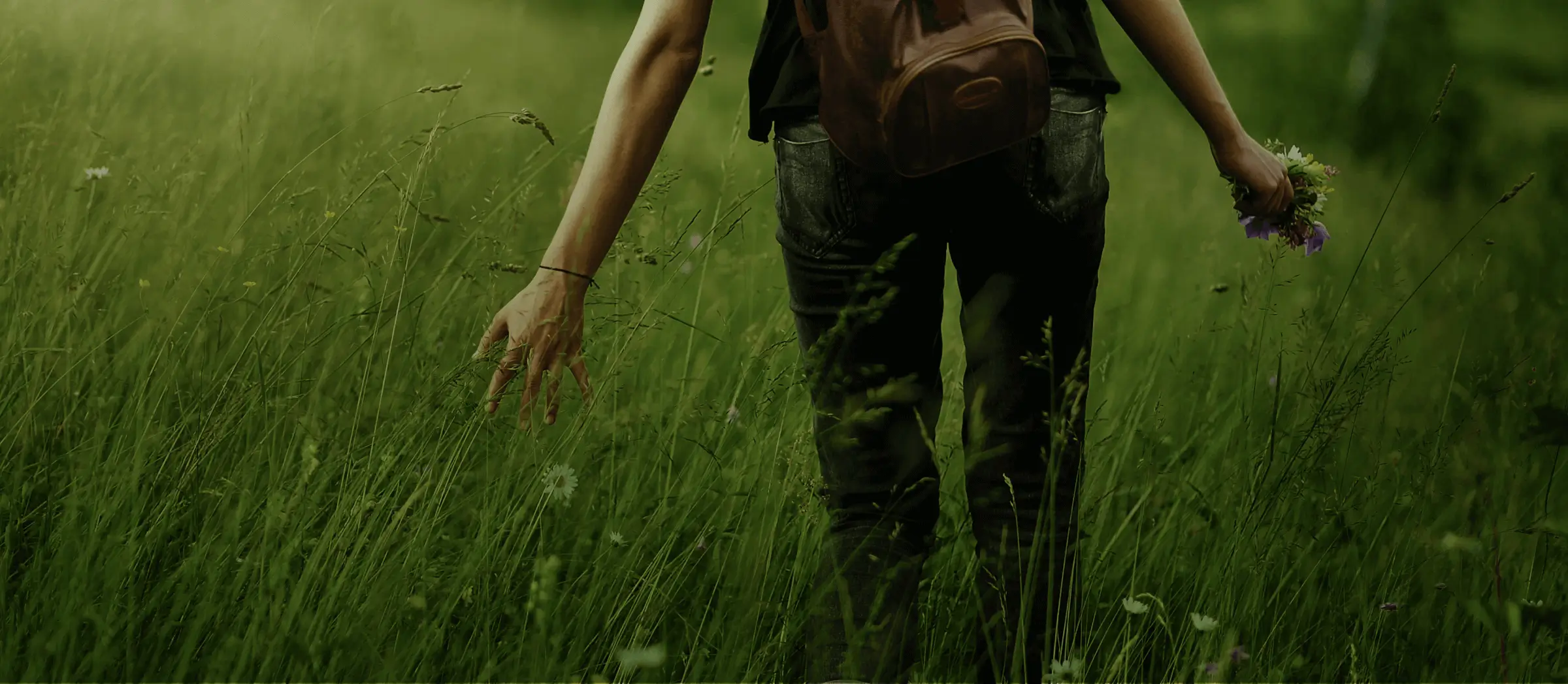 A woman walks through tall grass, holding flowers.