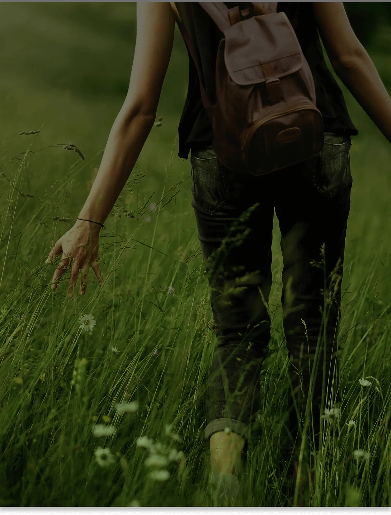 A woman walks through tall grass, holding flowers.